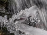 Teledetail der glitzernden Eisfiguren an Ast bei Kaskade im Steinbach
